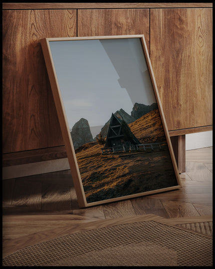 Ein gerahmtes Poster von einer kleinen Kapelle in den Dolomiten bei Sonnenuntergang, an einer Holzkommode angelehnt und stehend auf dem Holzboden