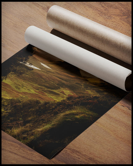 Ein Poster von einer kargen, grünen Berglandschaft im Sonnenuntergang, gerollt auf einer Holzoberfläche liegend