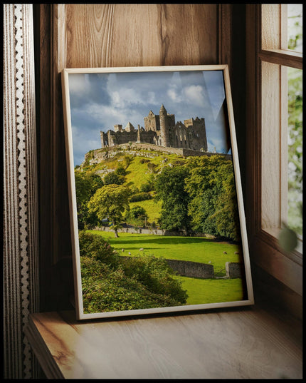 Ein gerahmtes Poster von den Ruinen des Rock of Cashel auf einem Hügel in Irland, umgeben von grünen Wiesen und Bäumen, vor einem Fenster an die Wand angelehnt